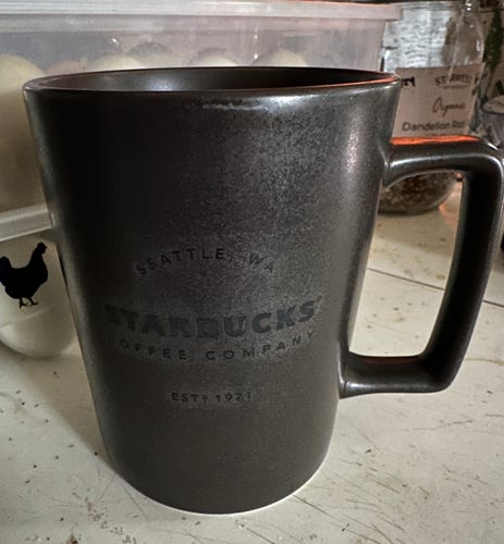 A close-up photo of a dark brown very generic Starbucks mug with a squareish handle. It's actually a very useful mug.
