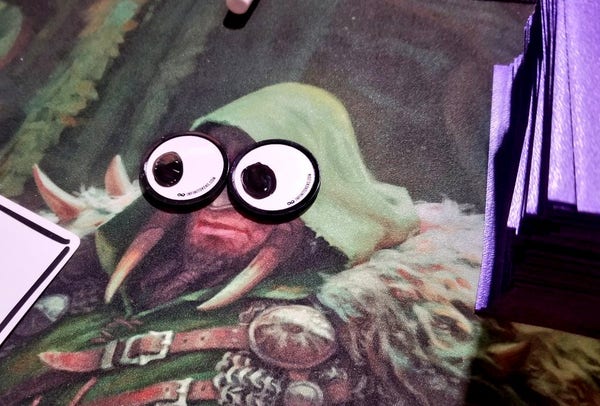 A playmat with Garruk on it. There are two InfiniTokens dry erase counters over his eyes with pupils drawn on them, so it looks like he has googly eyes.