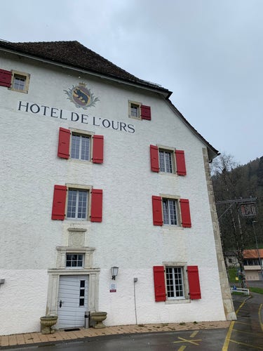 Seitenfassade des Hotel de l‘Ours in Bellelay. An der Fassade der Schriftzug und das Berner Wappen, links ein Wirtshausdingi aus Metall mit einem Bären.