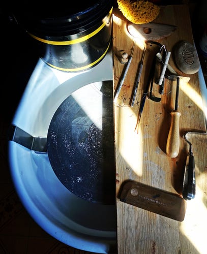 Foto ripresa dall'alto della mia pseudo postazione ceramica con tornio, secchio e una tavola di legno dove sono posati vari strumenti da ceramista. 
