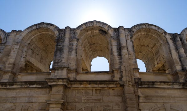 Three arches from the ruins of the arena in Arles. The sun is behind the arena, so the arches are in the shade and the sky behind a pellucid, pale blue.