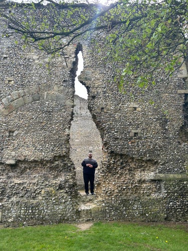 A man standing behind a wide hole/crack in the ruins, eating a bag of Pom bears. 