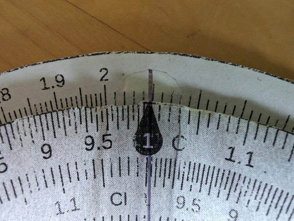 Closeup of a homemade circular slide rule showing 2.09 on the outer D scale above 1 on the inner C scale.