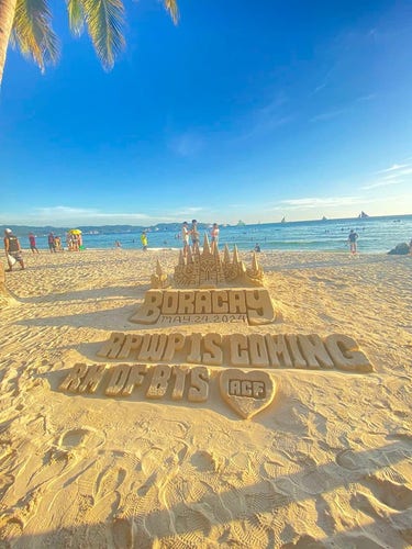 Sandcastle art in Boracay, with the water in the background. There is a sandcastle with "Boracay" written at the base, with the date May 24, 2024 (RM's album release). Then in front of that are raised letters that say "RPWP is coming. RM of BTS" with a heart enclosing the letters ACF (for ARMY Cavite Fanbase).