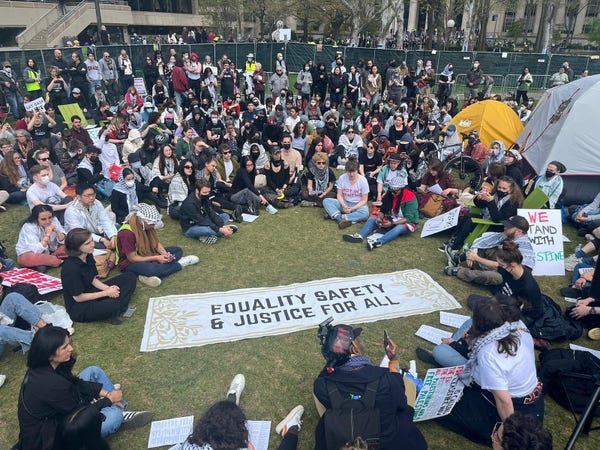 crowd gathered on grass around a banner that says Equality Safety & Justice For All