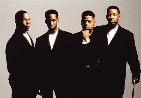 A photo of the 4 members of the group standing with dark suit on and white shirts. 