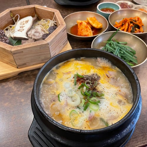 Gorąca, bulgocząca koreańska zupa podawana w kamiennym garnku z dodatkami takimi jak kimchi i warzywa na drewnianym stole.