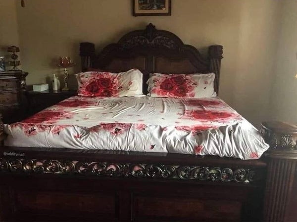 A large wooden double bed with white pillows and covers decorated with large red roses has the unfortunate effect of looking like bloodstained sheets. 