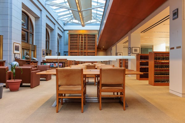 Looking across a row of tables and chairs at the library inside James Browning Ninth Circuit Courthouse in San Francisco. The library is modern in design decorated with varied browns and beiges, contrasting with cool gray stone on the outer walls. 