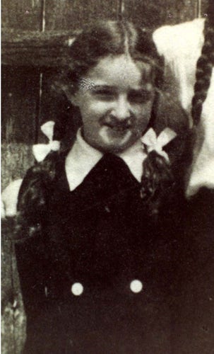 A young girl photo. SHe is smiling. She has long hair styled in braids. She has two ribbons on them. She seems to be wearing a school uniform.