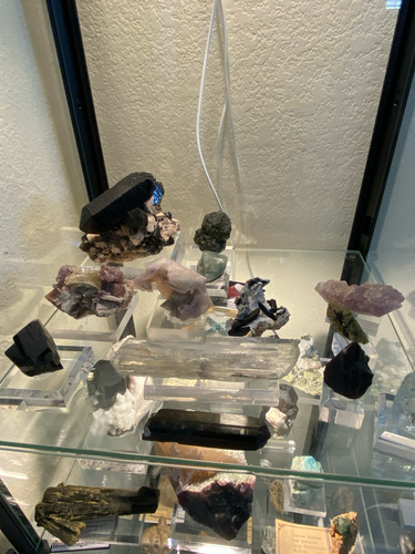 This shelf has a mix of stuff. In the back there’s a cool smoky quartz matrix piece from Dinkey Lakes, and a green garnet from Baja. In front of that there’s a bent tourmaline from the Himalaya Mine, a corroded montmorillonite quartz from the White Queen Mine, and a floater amethyst from Shaver Lake, a big spodumene, and several other Baja pieces. 