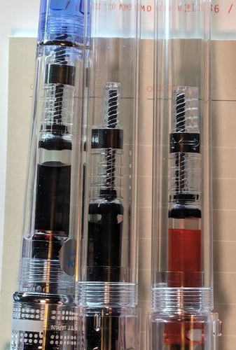 Three clear "demonstrator" fountain pens side-by-side: A Pilot Prera and two Pilot Kakunos. Only the main bodies of the pens are visible with a converter inside.

Each of the three pens has a Pilot CON-40 converter inside which is almost completely full of ink.

From left to right the ink colors are:

- Pilot Iroshizuku Yama-Budo (Purple)
- Diamine Writer's Blood (Dark Red)
- Diamine Sunshine Yellow (Yellow with a slight orange tone)