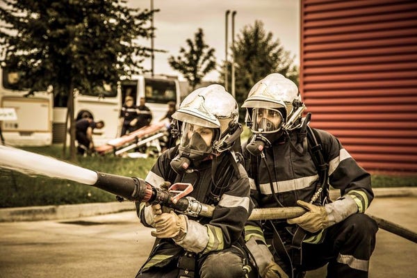 Sapeurs-pompiers à l'entrainement, mettant en oeuvre une lance à incendie
