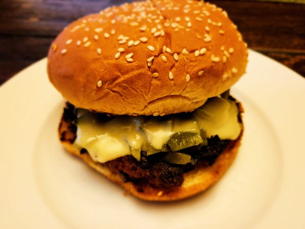 A burger topped with chopped roasted green chiles and white cheddar cheese.