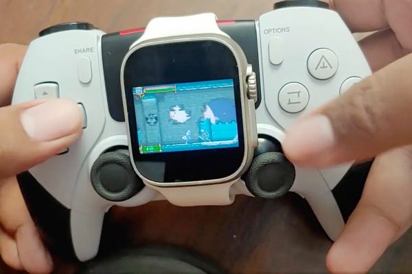 A Apple Watch displaying a retro-style video game strapped to a game controller held by hands.
